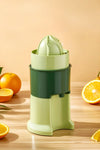 Green manual juicer on a wooden surface with oranges around it